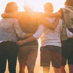 Group of four people hugging outdoors while the sun sets
