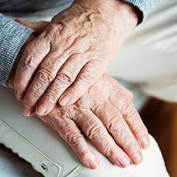 Elderly person crossing their hands over their leg