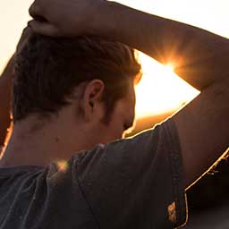 Man outdoors while the sun sets with his hands on his head