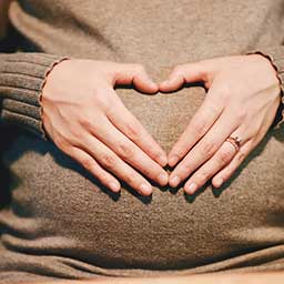 Mother placing hands in heart shape over pregnant belly